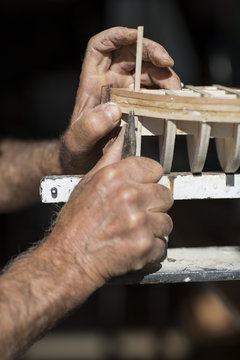 handcrafted craftwork of a wooden boat model / old man working on creating a wooden model of a boat  