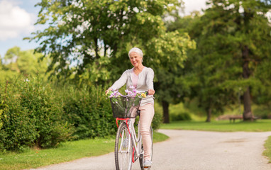 happy senior woman riding bicycle at summer park