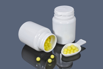 Yellow dragee balls of vitamins in the measuring spoon and medical plastic containers