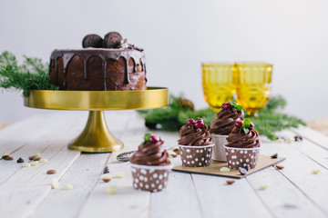 Dark chocolate cake with cookies and cupcakes berries on white wooden background