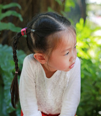 Adorable little asian girl looking out and sitting in the garden with background of tropical trees in the park.