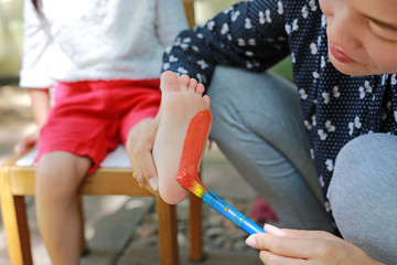 Mother painted foot with color green-orange for her daughter in the park. Focus at child foot.