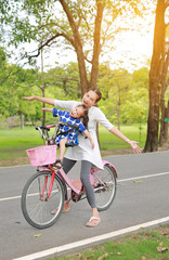 Happy asian mother and daughter arm stretch and riding bicycle together in park.