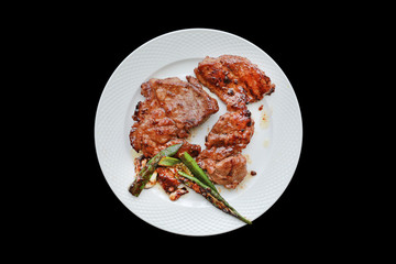Pork steak with vegetables in white plate isolated on black background.