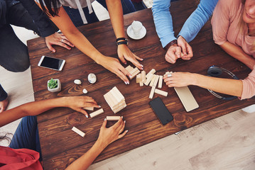 Top view creative photo of friends sitting at wooden table. Friends having fun while playing board...