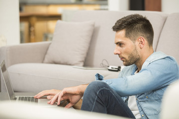 Fototapeta premium Young man in living-room using laptop computer