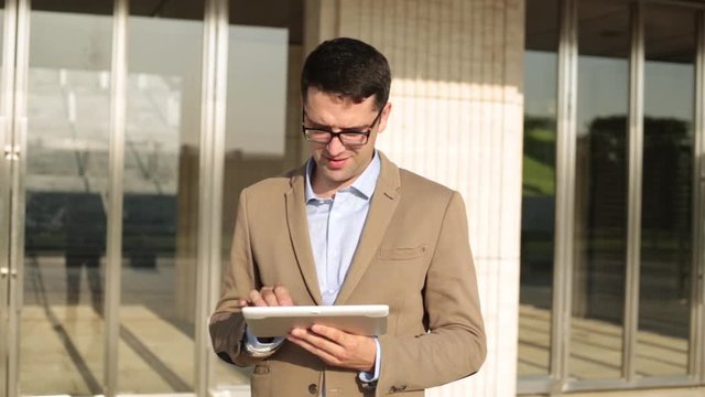 Businessman uses a tablet computer on the background of an office building.