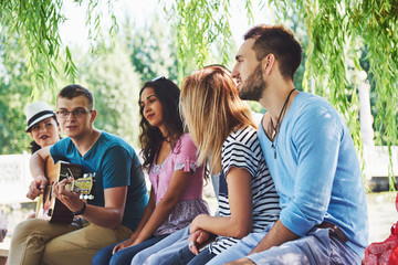 Group of happy friends with guitar. While one of them is playing guitar and others are giving him a round of applause