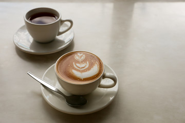 Hot coffee with flower shape latte art and tea on marble desk with copy space