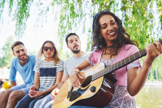 Group Of Happy Friends With Guitar. While One Of Them Is Playing Guitar And Others Are Giving Him A Round Of Applause