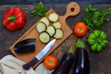 Sliced eggplant, tomato and pepper on wooden cutting board. Preparation for cooking ratatouille or stew