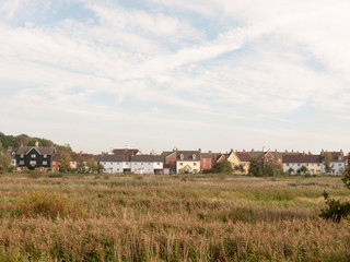 row of houses on coast edge behind field across the way sky and grass