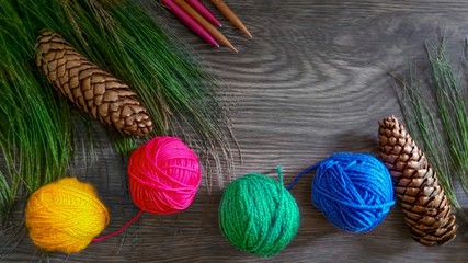 Multicolored yarn balls, needles for knitting, pine cone and Christmas tree branch on wood...