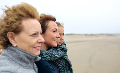 Closeup of three generations female looking at sea on the beach in autumn. Background focus on young woman and child
