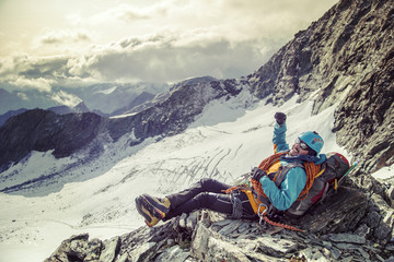 Climber with big smile on his face taking a break and enjoying a view from the mountain top,  with hand raised in the sky