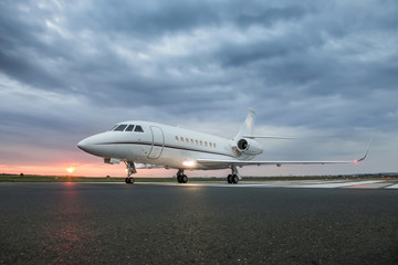 Fototapeta na wymiar Modern advanced private business jet ready to take off with sunrise in the background and clouds above airplane 