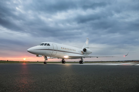 Modern Advanced Private Business Jet Ready To Take Off With Sunrise In The Background And  Clouds Above Airplane  