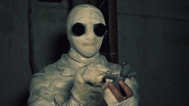 people being in bandages in a dark, abandoned building holding a voodoo doll for ritual