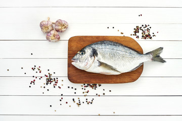Fresh dorado fish on wooden cutting board with garlic and peppercorns. Top view, copy space