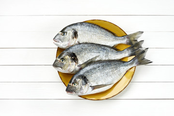 Raw dorado fish on yellow plate on white wooden background. Top view, copy space