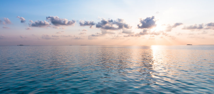 Sunset over the tropical islands. A gentle watercolor sunset over the ocean. The sun's rays shine through the clouds.