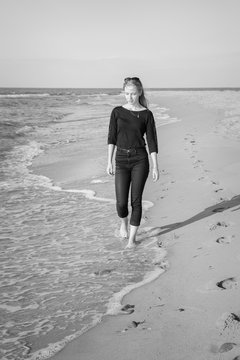 sad blond barefoot woman walking at sunny sea beach, monochrome
