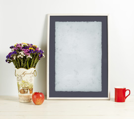 White frame mockup with plant pot, mug and apple on wooden shelf.