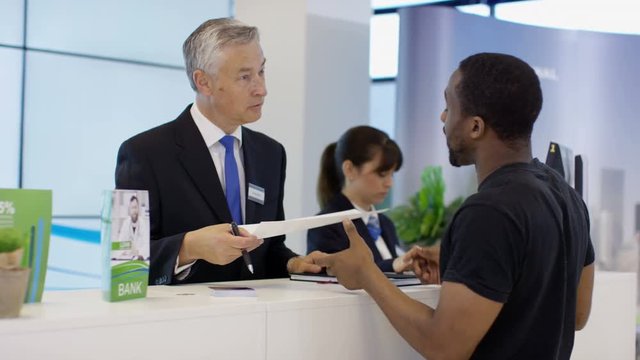  Friendly bank worker at service desk assisting customers with enquiries