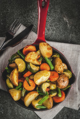 Skillet with  fried seasonal autumn vegetables (zucchini, potatoes, carrots, beans), on black stone table copy space top view