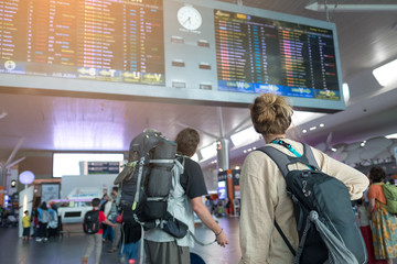 Young couple with backpack in airport near flight timetable