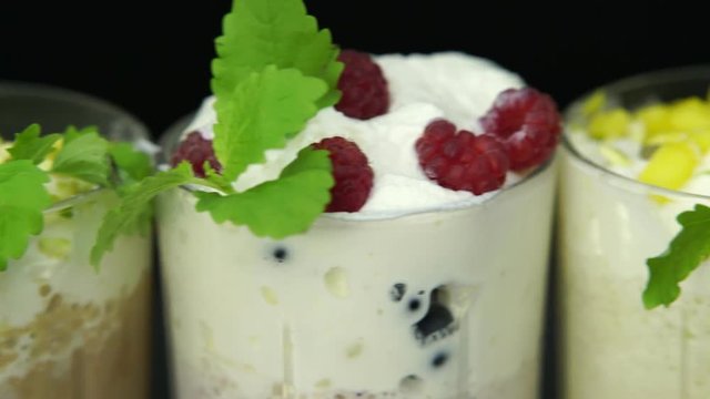 Delicious milkshakes with cream, berries, fruits and mint leaves close up on black background.