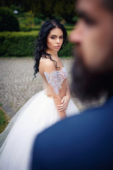 Fototapeta na wymiar A beautiful brunette in a wedding dress and a bearded bride walking around an ancient castle