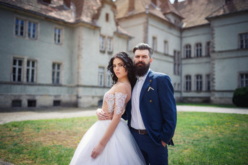 Naklejka premium A beautiful brunette in a wedding dress and a bearded bride walking around an ancient castle