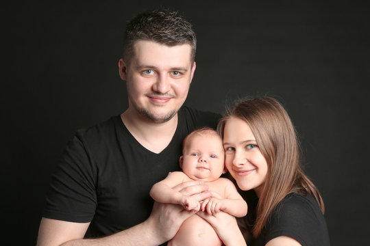 Happy young family holding newborn on black background