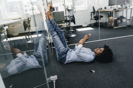 Young woman lying on the floor in office checking cell phone