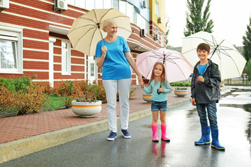 Fototapeta na wymiar Elderly woman and little children walking with umbrellas on street