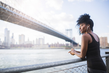 USA, New York City, Brooklyn, woman listening to music near Manhattan Bridge