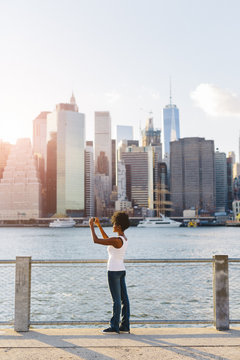 USA, New York City, Brooklyn, woman standing at the waterfront taking cell phone picture