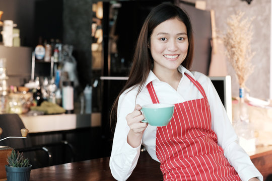 Young asian women Barista holding coffee cup with smiling face at cafe counter background, small business owner, food and drink industry concept
