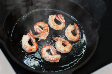 Big king prawns are fried in a black frying pan.