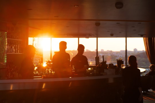 Silhouettes of people against the setting sun in a bar on the top floor of a skyscraper