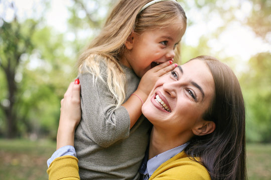 Mother and daughter outdoors in a meadow. Daughter whispering to her mother secret. - Powered by Adobe