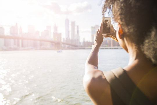 USA, New York City, Brooklyn, woman taking cell phone picture of skyline