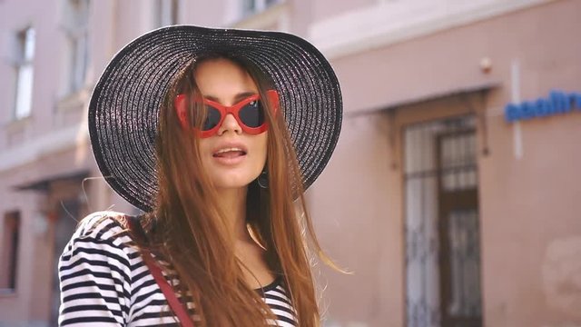 Woman in black hat and red sunglasses smiles whirling on the street