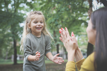 Mother and daughter on meadow. Mother and daughter playing with hands. Focus on little girl.