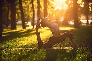 Beautiful young woman practices yoga asana King Pigeon pose rajakapotasana in the park at sunset