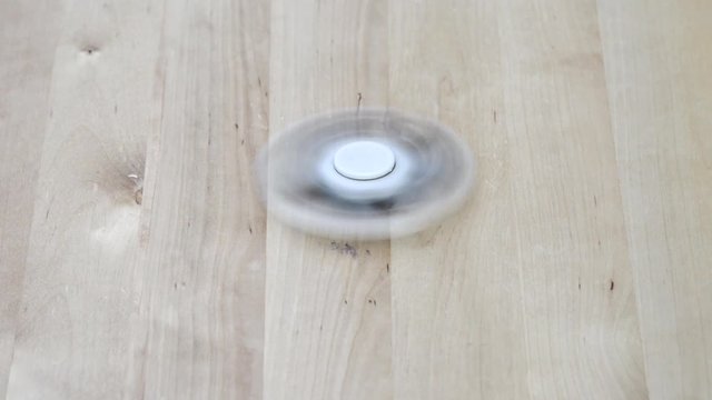 A white fidget spinner stress relieving toy spinning on wooden background