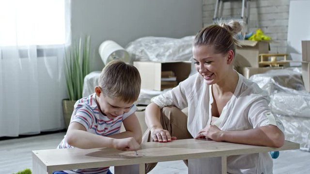 PAN of little boy putting screws into wooden shelf while proud mother watching and smiling, then high-fiving and laughing