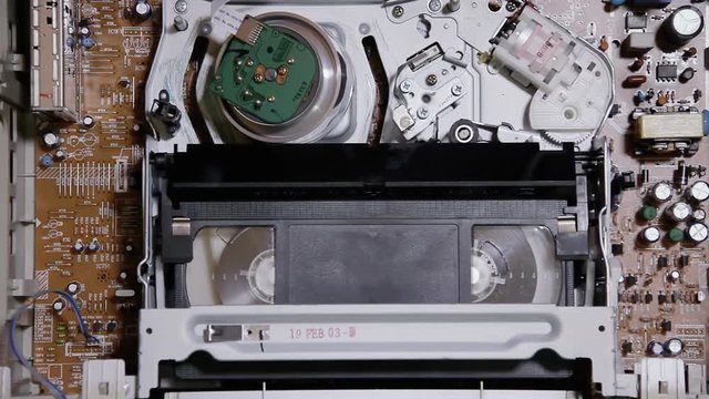 Inserting and removing a VHS tape from an open VCR. Above shot of the inner mechanism.
