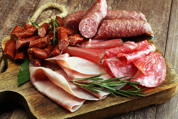 Marble cutting board with prosciutto, bacon, salami and sausages on wooden background. Meat platter